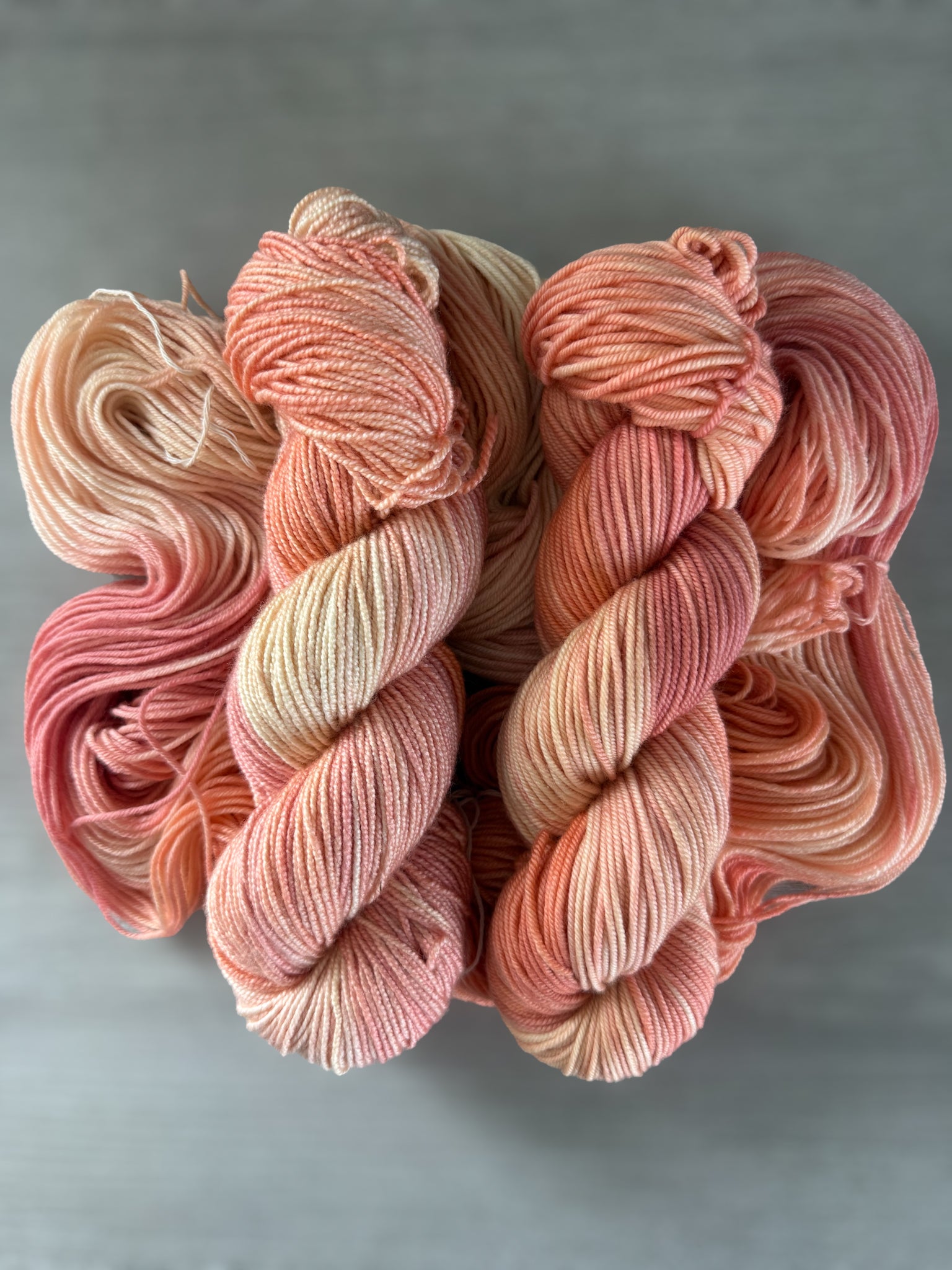 Ethically sourced Whispering Petals hand-dyed merino wool yarn in soft peach, ivory, and light rose hues.