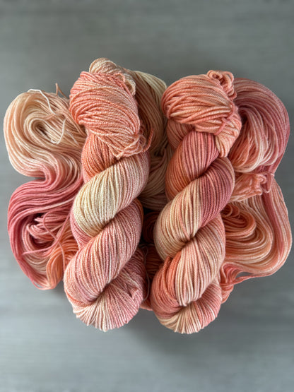 Ethically sourced Whispering Petals hand-dyed merino wool yarn in soft peach, ivory, and light rose hues.