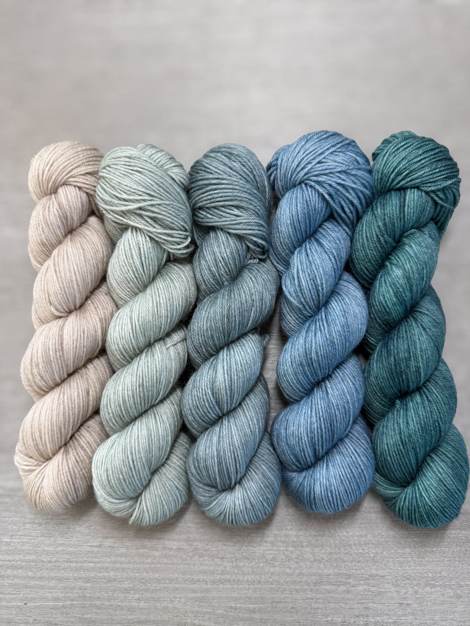 Ethically sourced merino wool mini skeins in soft sage, muted blues, and forest greens.