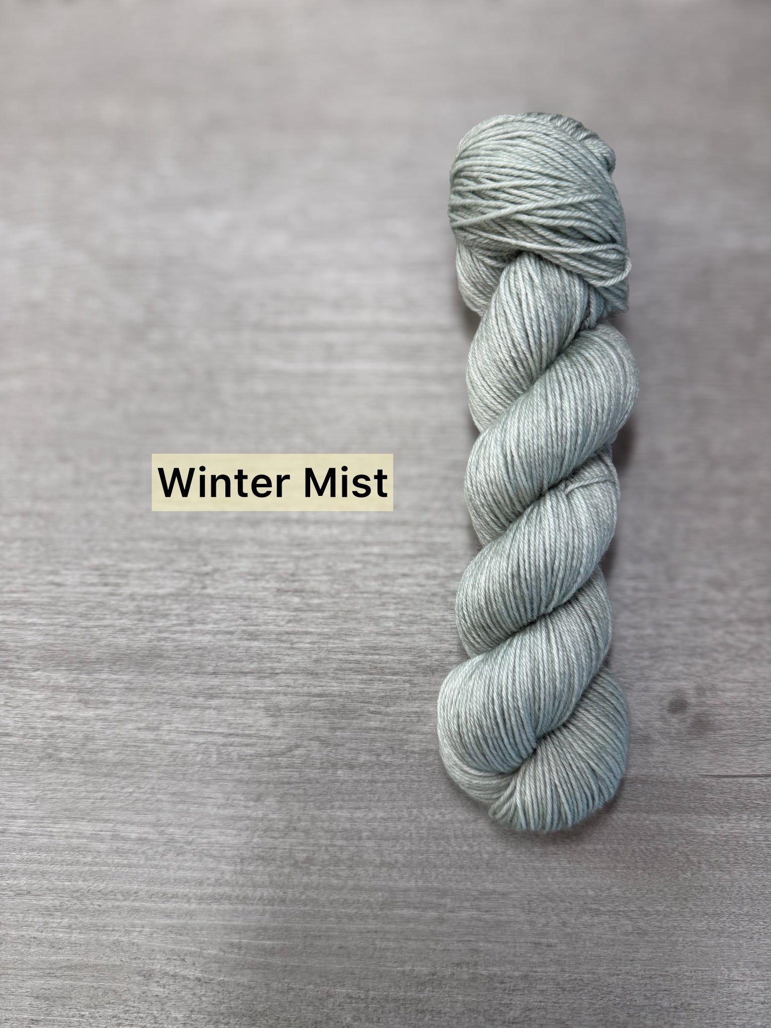 Ethically sourced merino wool yarn in "Winter Mist," a soft sage green, hand-dyed fingering weight skein.